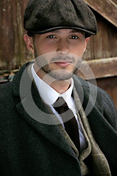 Handsome English gangster dressed in waistcoat and jacket sitting and looking at camera, leaning on gate