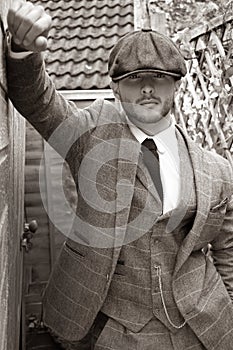 Handsome English gangster leaning on brick wall in back streets of birmingham