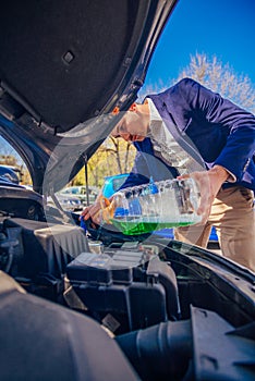 Handsome entrepreneur business casually dressed is pouring some antifreeze in his car`s engine