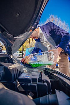 Handsome entrepreneur business casually dresses is pouring some antifreeze in his car`s engine