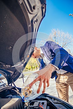 Handsome entrepreneur business casually dresses is pouring some antifreeze in his car`s engine