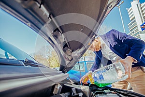 Handsome entrepreneur business casually dresses is pouring some antifreeze in his car`s engine