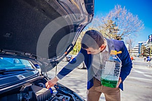 Handsome entrepreneur business casually dresses is pouring some antifreeze in his car`s engine