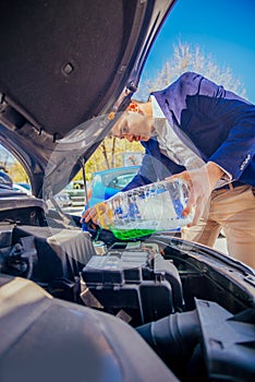 Handsome entrepreneur business casually dresses is pouring some antifreeze in his car`s engine