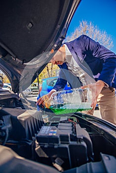 Handsome entrepreneur business casually dresses is pouring some antifreeze in his car`s engine