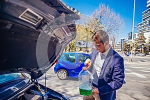 Handsome entrepreneur business casually dresses is pouring some antifreeze in his car`s engine