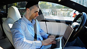 Handsome entrepreneur working on notebook while riding an autonomous self driving electric car at urban road. Male