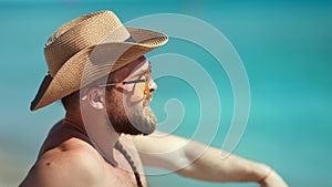 Handsome European guy in sunglasses and hat relaxing on beach at seascape background