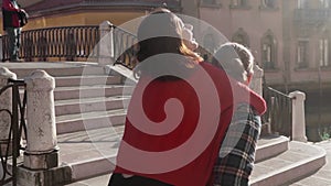 Handsome european man carrying on his back gorgeous asian woman in the streets of Venice. Young hipster couple in love