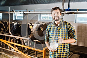 handsome farmer holding jug of milk in stable and looking