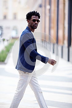 Handsome fashion African American man walks down the street in stylish attire white pants, blue blazer. Fashionable