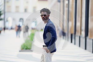 Handsome fashion African American man walks down the street in stylish attire white pants, blue blazer. Fashionable