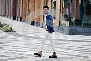 Handsome fashion African American man walks down the street in stylish attire white pants, blue blazer, and loafers