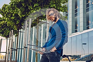 A handsome fashionable bearded male with long hair dressed in stylish clothes, working with a tablet computer after