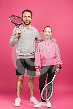 handsome father and daughter holding tennis rackets and ball, isolated