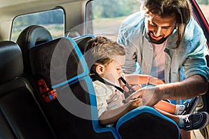 handsome father fastening son in safety seat photo