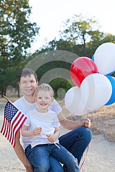 handsome father holding colorful balloons and his little son holding american flag celebrating 4th of July