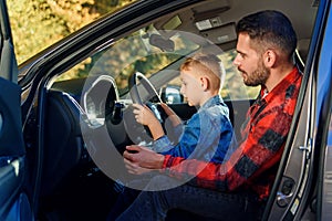 Handsome father pointing on something while teaching teen son driving car