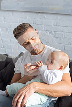 handsome father sitting on couch and feeding baby daughter