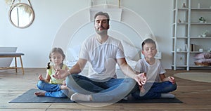 Handsome father sitting in lotus position with adorable children on his sides, meditating in a quiet calm environment