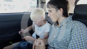 Handsome father with son sit in car seat and playing on smart phone while having car ride in backseat