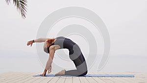 Handsome female doing hatha yoga asana at sea on foggy sunrise