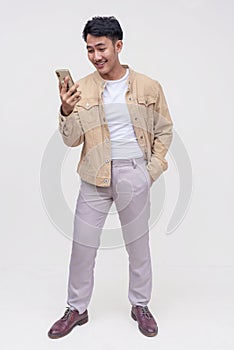 A handsome FIlipino guy in a khaki jacket, white shirt and light gray pants. Checking his phone for messages. Whole body photo, photo