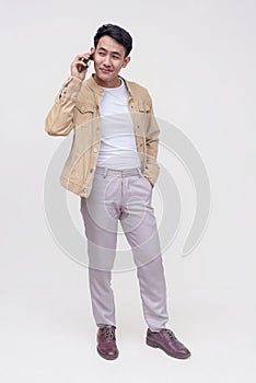 A handsome FIlipino guy in a khaki jacket, white shirt and light gray pants. Holding a phone talking to someone. Whole body photo
