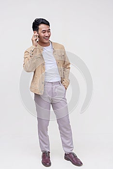 A handsome FIlipino guy in a khaki jacket, white shirt and light gray pants. Holding a phone talking to someone. Whole body photo