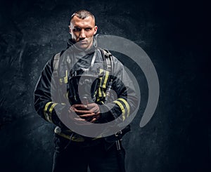 A handsome fireman wearing protective uniform holding an oxygen mask and looking at a camera.