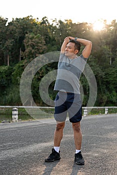 A handsome, fit Asian man in sportswear is stretching his arms, warming up before running in a park
