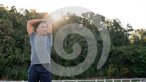 A handsome, fit Asian man in sportswear is stretching his arms, warming up before running in a park