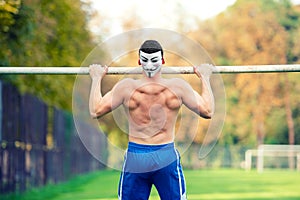 Handsome fit caucasian man, shirtless, doing pull ups in park, outdoors. Fitness training on a summer sunny day