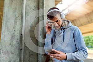 Handsome fit man taking a break after intensive training outdoors, texting on his smart phone wearing headphones