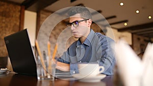 Handsome freelancer businessman in glasses diligently working on laptop in cafe is constantly distracting by annoying