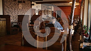 Handsome freelancer businessman in glasses diligently working on laptop in cafe. Man typing on keyboard and searches new