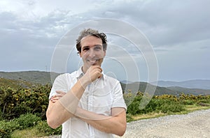 a handsome French or Spaniard man in a white shirt stands against the backdrop of mountains photo