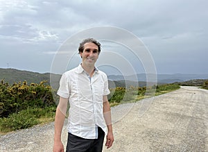 a handsome French or Spaniard man in a white shirt stands against the backdrop of mountains photo