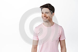 Handsome friendly man in t-shirt looks aside with pleased smile, satisfied with promo, looking at logo and nod in
