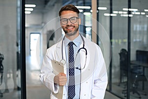 Handsome friendly young doctor on hospital corridor looking at camera, smiling