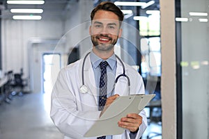 Handsome friendly young doctor on hospital corridor looking at camera, smiling