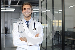 Handsome friendly young doctor on hospital corridor looking at camera, smiling