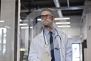 Handsome friendly young doctor on hospital corridor looking at camera, smiling