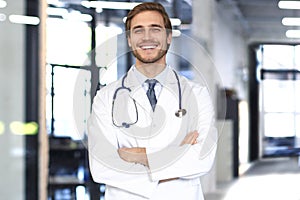 Handsome friendly young doctor on hospital corridor looking at camera, smiling