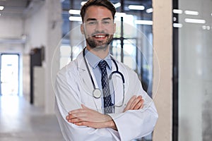 Handsome friendly young doctor on hospital corridor looking at camera, smiling