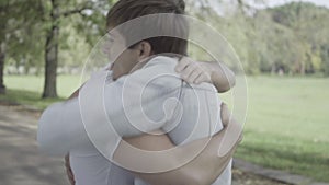 Handsome friends meeting in sunny summer park outdoors. Side view portrait of happy excited young Caucasian men hugging