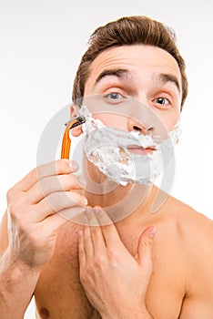 Handsome funny man with shaving foam on his face and razor
