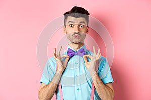 Handsome and funny young man pucker lips for kiss, showing his classy bow-tie, wearing clothes for party, standing on