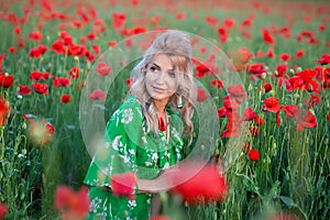 A handsome girl with long hair and natural skin, standing in a fiel of red poppies and holding a red poppy in hands, on nature