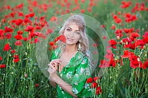 A handsome girl with long hair and natural skin, standing in a fiel of red poppies and holding a red poppy in hands, on nature